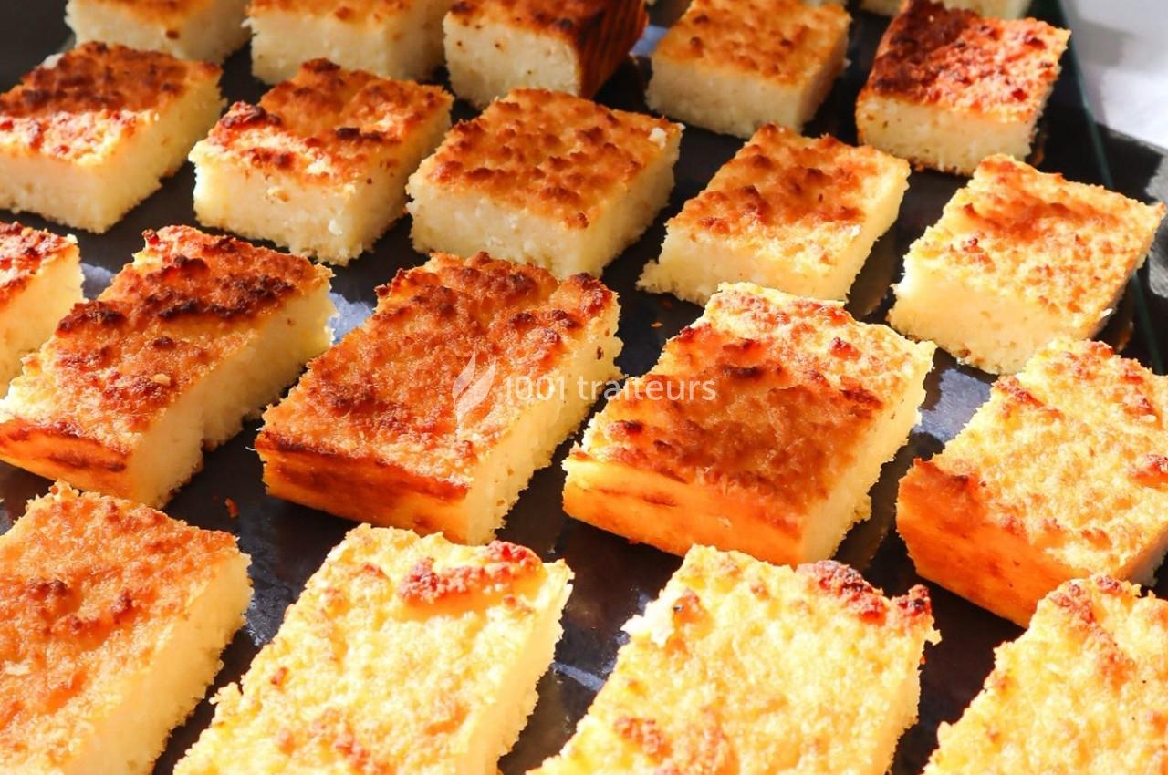 Carrés de gâteau à la noix de coco dorés, alignés sur une plaque de cuisson noire.