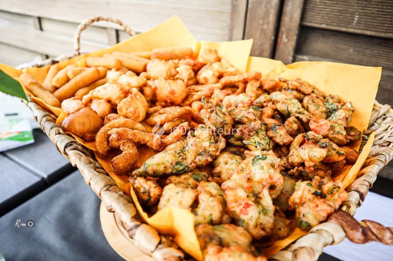 Assortiment de beignets salés variés présentés dans un panier en osier garni de papier jaune.