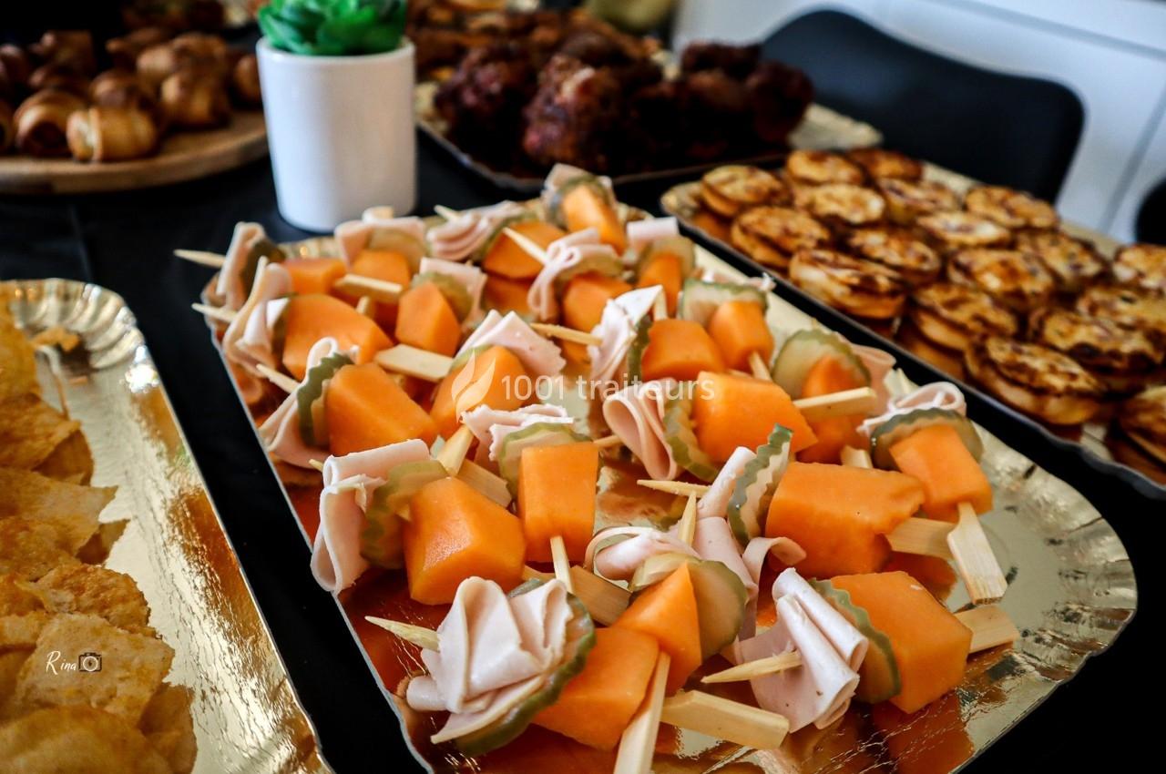 Plateau de brochettes apéritives avec morceaux de melon, jambon et fromage, entouré d'autres plats variés.