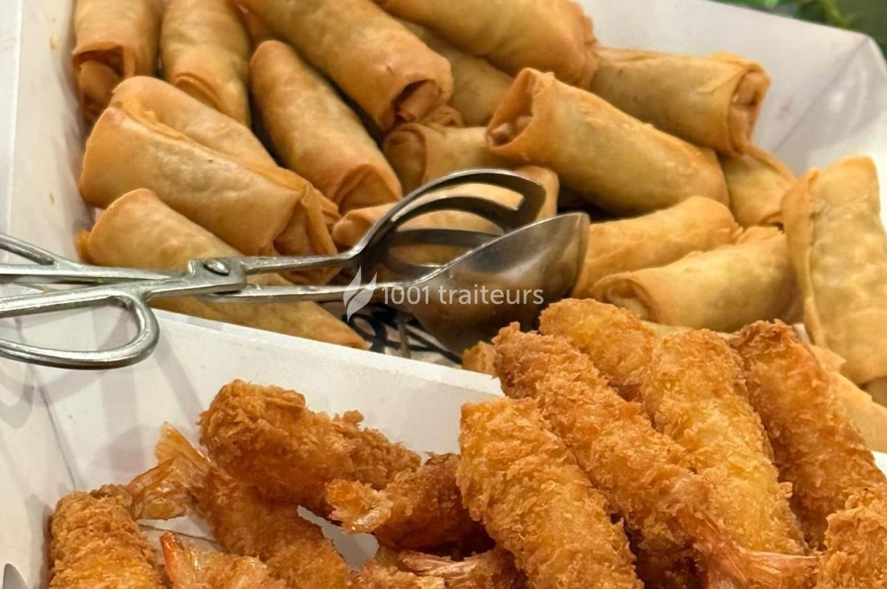 Assortiment de nems dorés et de crevettes panées disposés dans un plateau avec des pinces en métal.