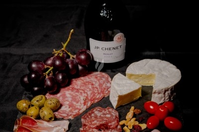Plateau de charcuterie et fromages avec fruits, légumes, et une bouteille de vin rouge, sur une table en extérieur la nuit.
