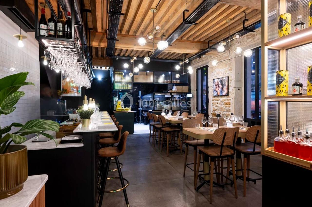 Intérieur d'un restaurant moderne avec bar, tables en bois, éclairage suspendu et murs en pierre apparente.