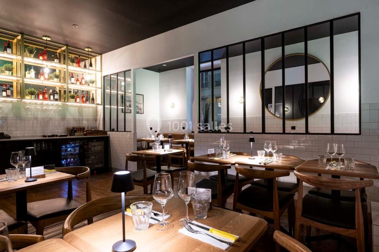 Salle de restaurant moderne avec tables en bois, chaises assorties, bar éclairé et miroir rond sur le mur.