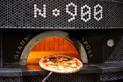 Pizza margherita sortant d'un four à bois avec une façade en mosaïque noire et l'inscription ’N° 900’.