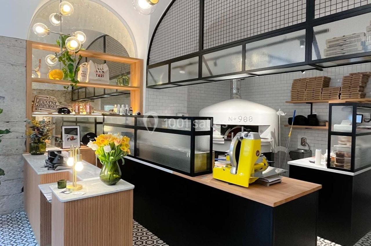 Intérieur d'une pizzeria moderne avec un four à pizza, un comptoir en bois et des décorations lumineuses.