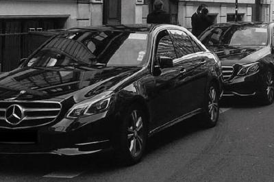 Alignement de véhicules noirs stationnés devant un bâtiment en pierre avec arcades, sous un ciel dégagé.