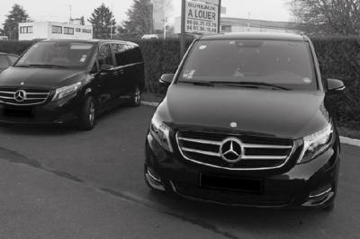 Alignement de véhicules noirs stationnés devant un bâtiment en pierre avec arcades, sous un ciel dégagé.