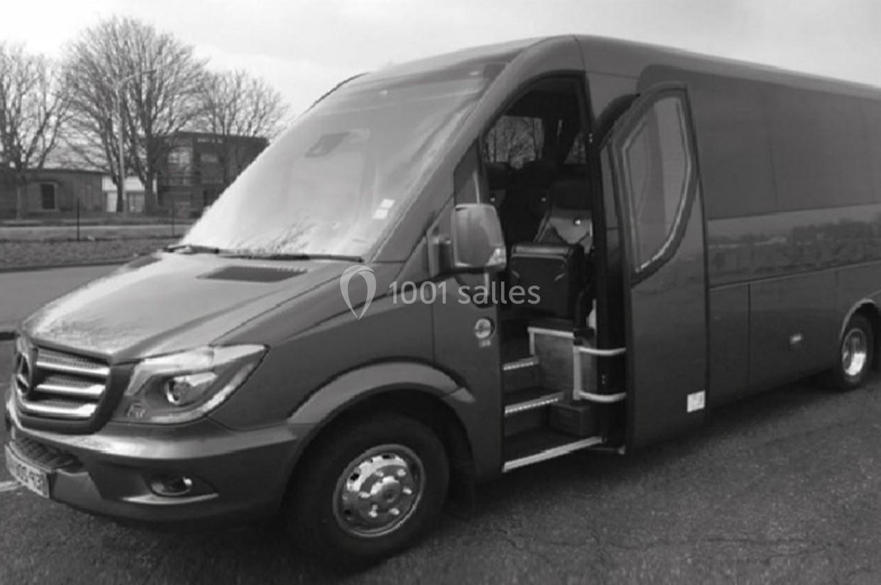Minibus stationné sur une route, porte latérale ouverte, avec des arbres visibles en arrière-plan.