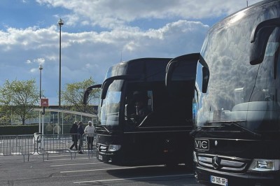 Alignement de véhicules noirs stationnés devant un bâtiment en pierre avec arcades, sous un ciel dégagé.