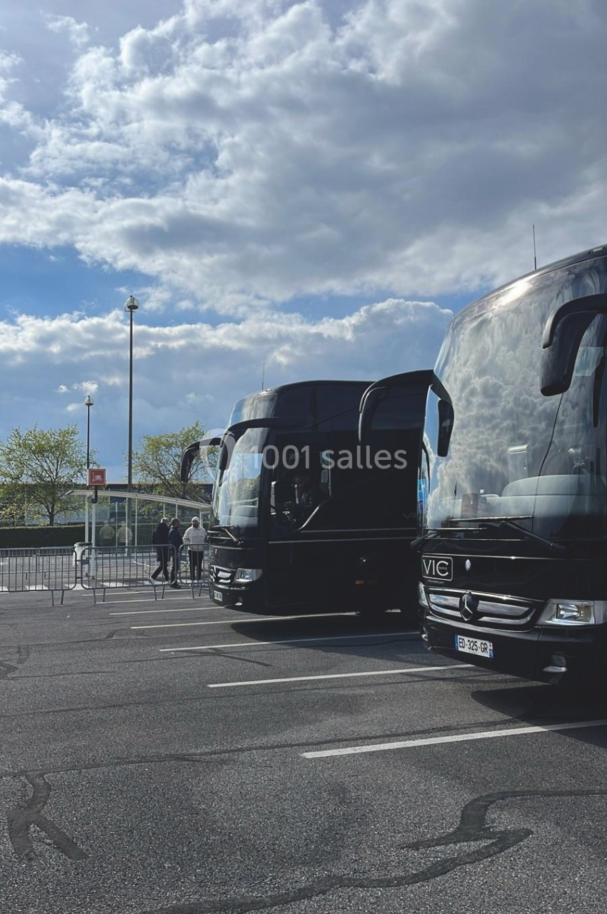 Deux bus noirs stationnés sur un parking sous un ciel partiellement nuageux.
