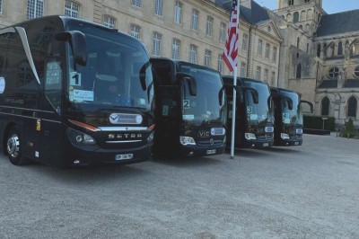 Alignement de véhicules noirs stationnés devant un bâtiment en pierre avec arcades, sous un ciel dégagé.