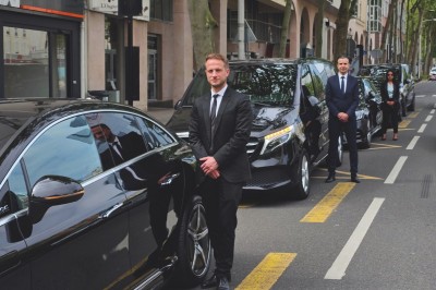 Alignement de véhicules noirs stationnés devant un bâtiment en pierre avec arcades, sous un ciel dégagé.