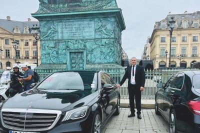 Alignement de véhicules noirs stationnés devant un bâtiment en pierre avec arcades, sous un ciel dégagé.