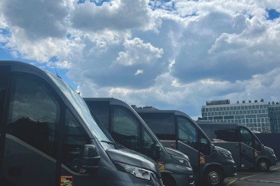 Alignement de véhicules noirs stationnés devant un bâtiment en pierre avec arcades, sous un ciel dégagé.