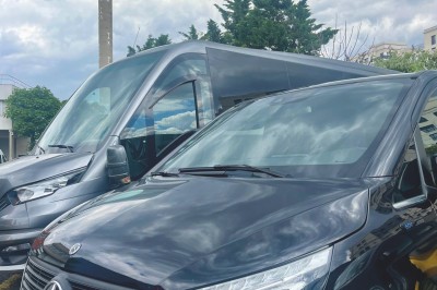 Alignement de véhicules noirs stationnés devant un bâtiment en pierre avec arcades, sous un ciel dégagé.