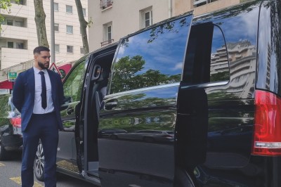 Alignement de véhicules noirs stationnés devant un bâtiment en pierre avec arcades, sous un ciel dégagé.