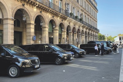 Alignement de véhicules noirs stationnés devant un bâtiment en pierre avec arcades, sous un ciel dégagé.