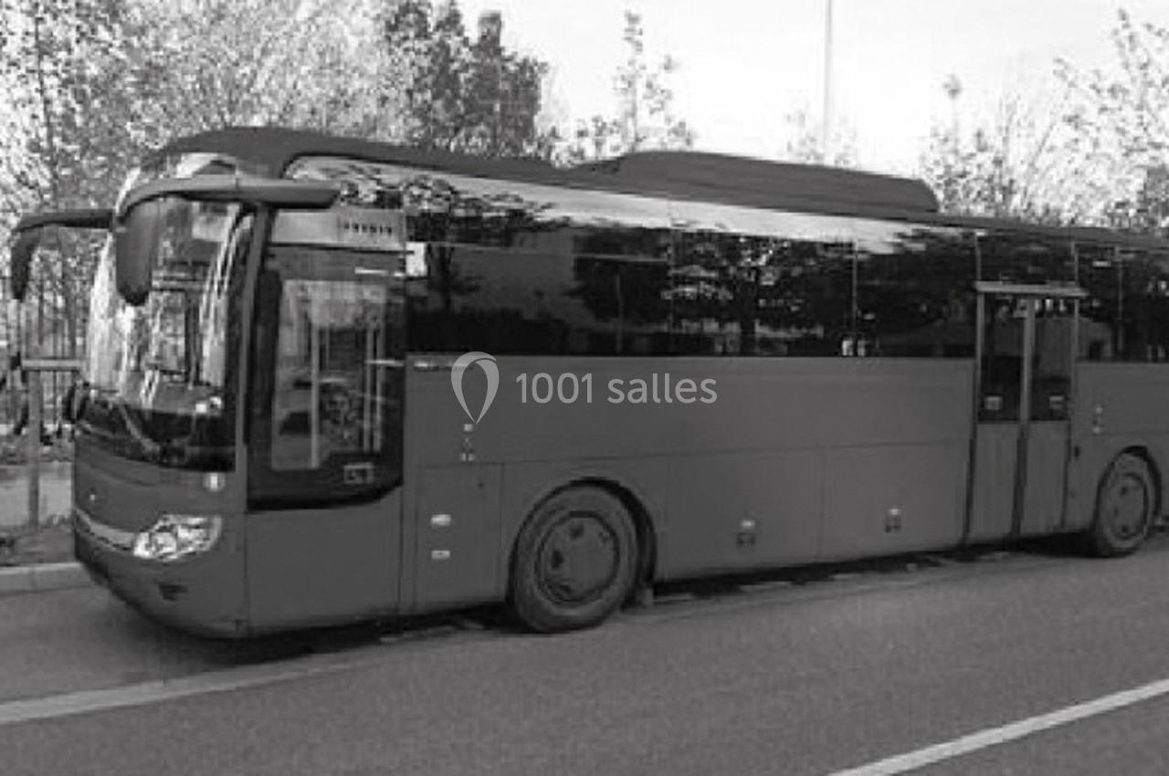Autocar stationné sur le bord d'une route, entouré d'arbres et de végétation en arrière-plan.