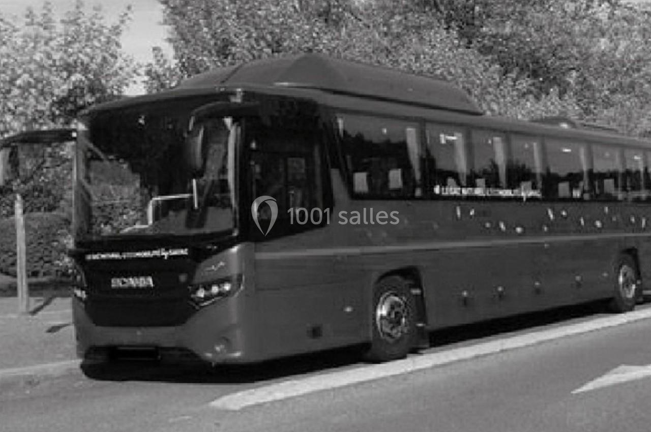 Autocar stationné près d'un trottoir, entouré d'arbres et d'un abribus en arrière-plan.