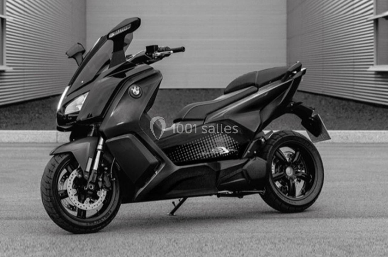 Scooter électrique moderne noir stationné devant un bâtiment aux murs métalliques.