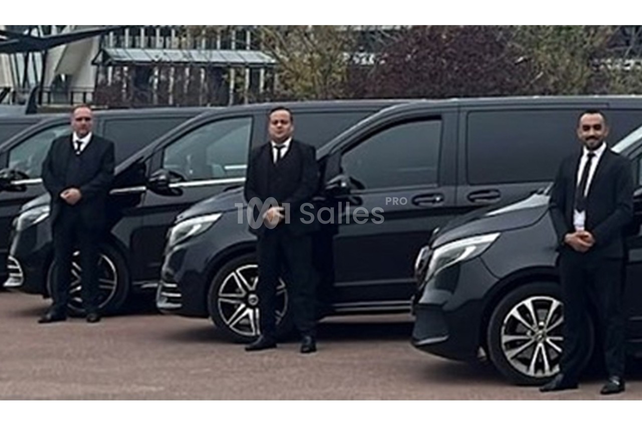 Trois hommes en costume noir se tiennent debout devant une rangée de vans noirs garés.