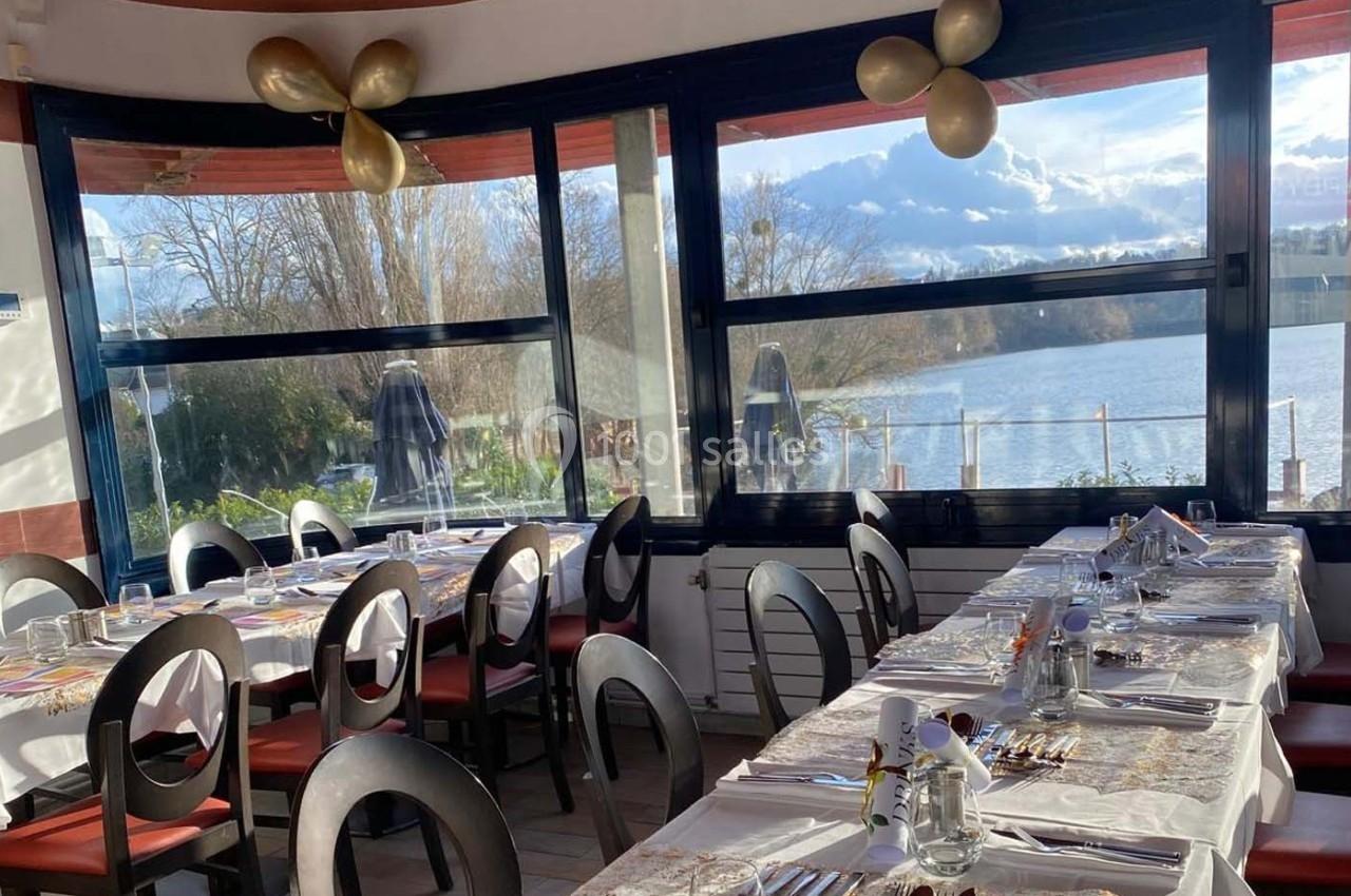 Salle de restaurant lumineuse avec tables dressées, vue sur un lac et décorations dorées au plafond.