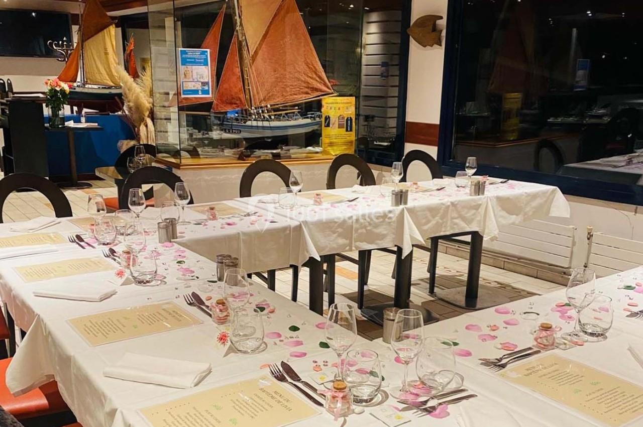 Tables dressées avec nappes blanches, menus, verres et décorations, dans un restaurant avec maquettes de voiliers en arrière…