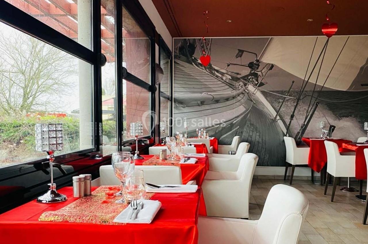 Salle de restaurant lumineuse avec tables dressées en rouge et blanc, décorée de motifs nautiques et cœurs suspendus.