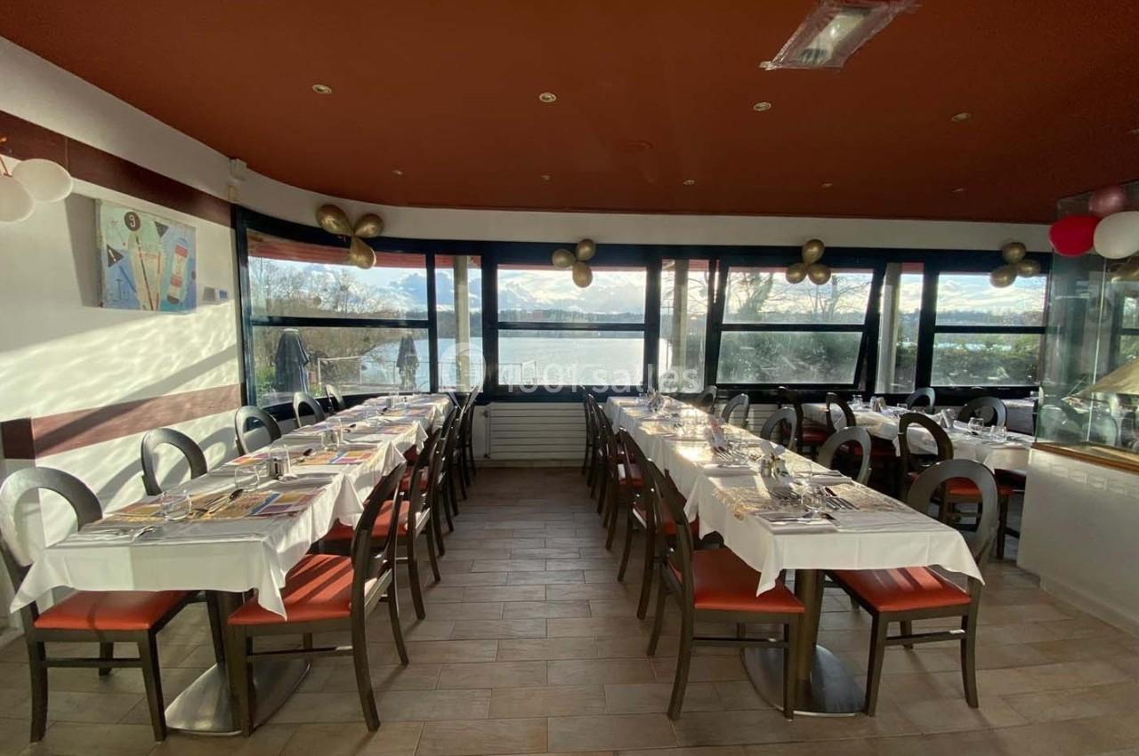 Salle de restaurant lumineuse avec tables dressées, grandes baies vitrées offrant une vue sur un paysage extérieur.