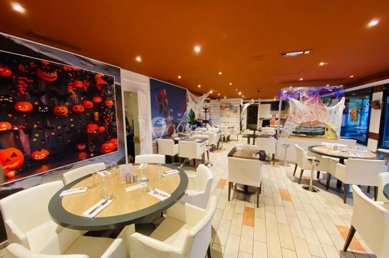 Salle de restaurant décorée pour Halloween avec des citrouilles lumineuses, toiles d'araignée et chaises blanches.