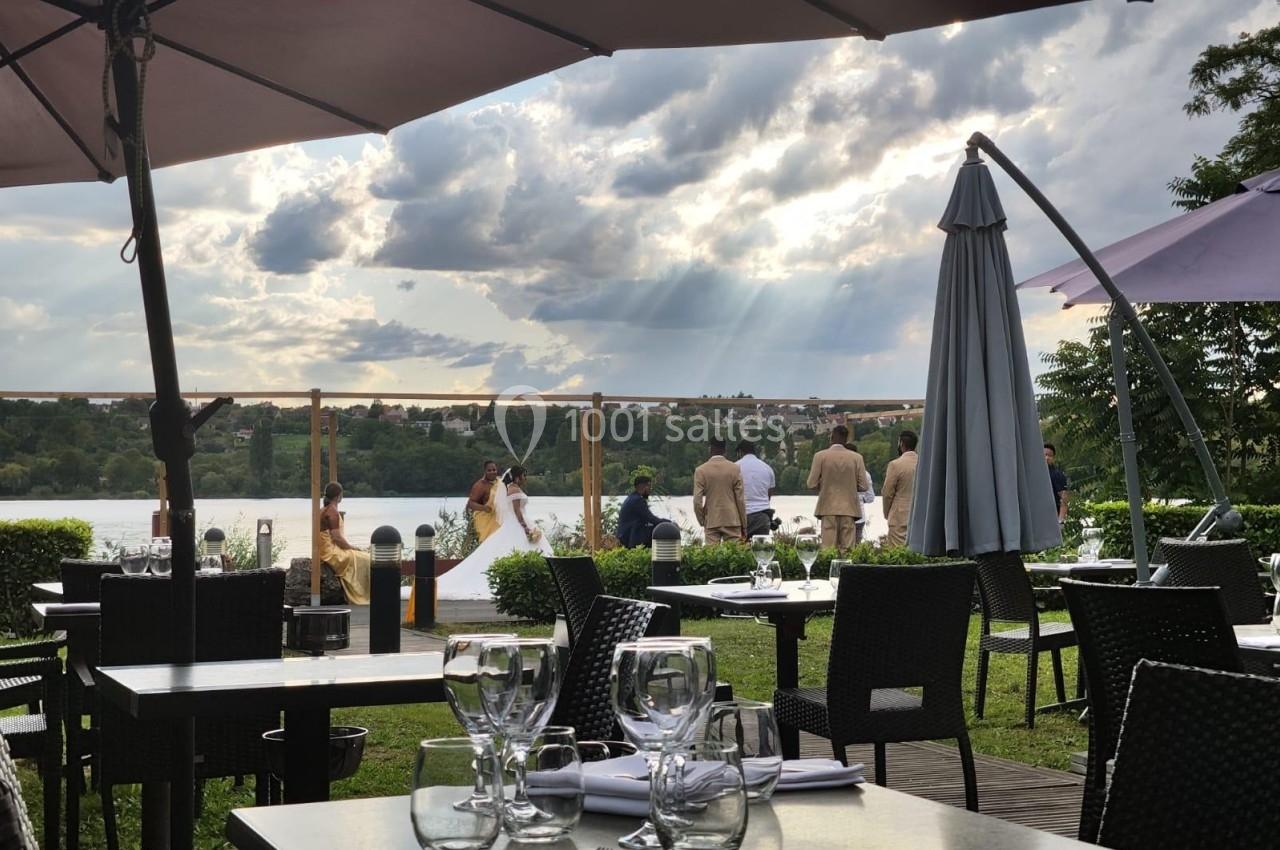 Terrasse d'un restaurant avec vue sur un lac, des tables dressées et un groupe de personnes près de l'eau.