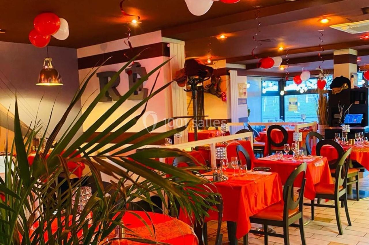 Salle de restaurant décorée avec des nappes rouges, des ballons suspendus et une lumière chaleureuse.