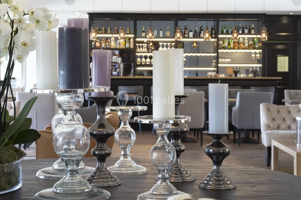 Bougies de différentes tailles et couleurs sur des chandeliers en verre et métal, avec un bar en arrière-plan.