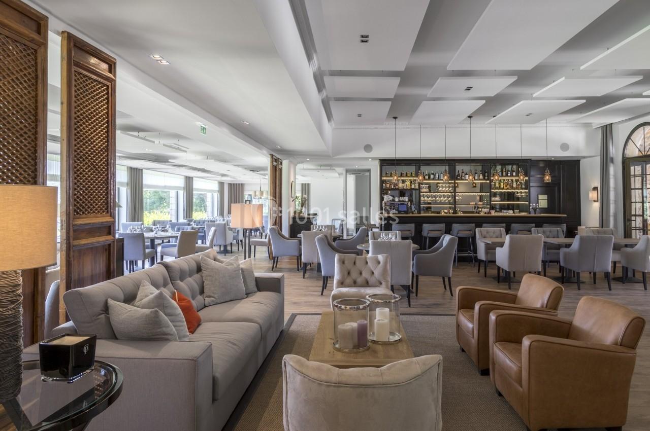 Salon élégant avec canapés, fauteuils en cuir, tables basses et bar en arrière-plan dans une ambiance lumineuse.