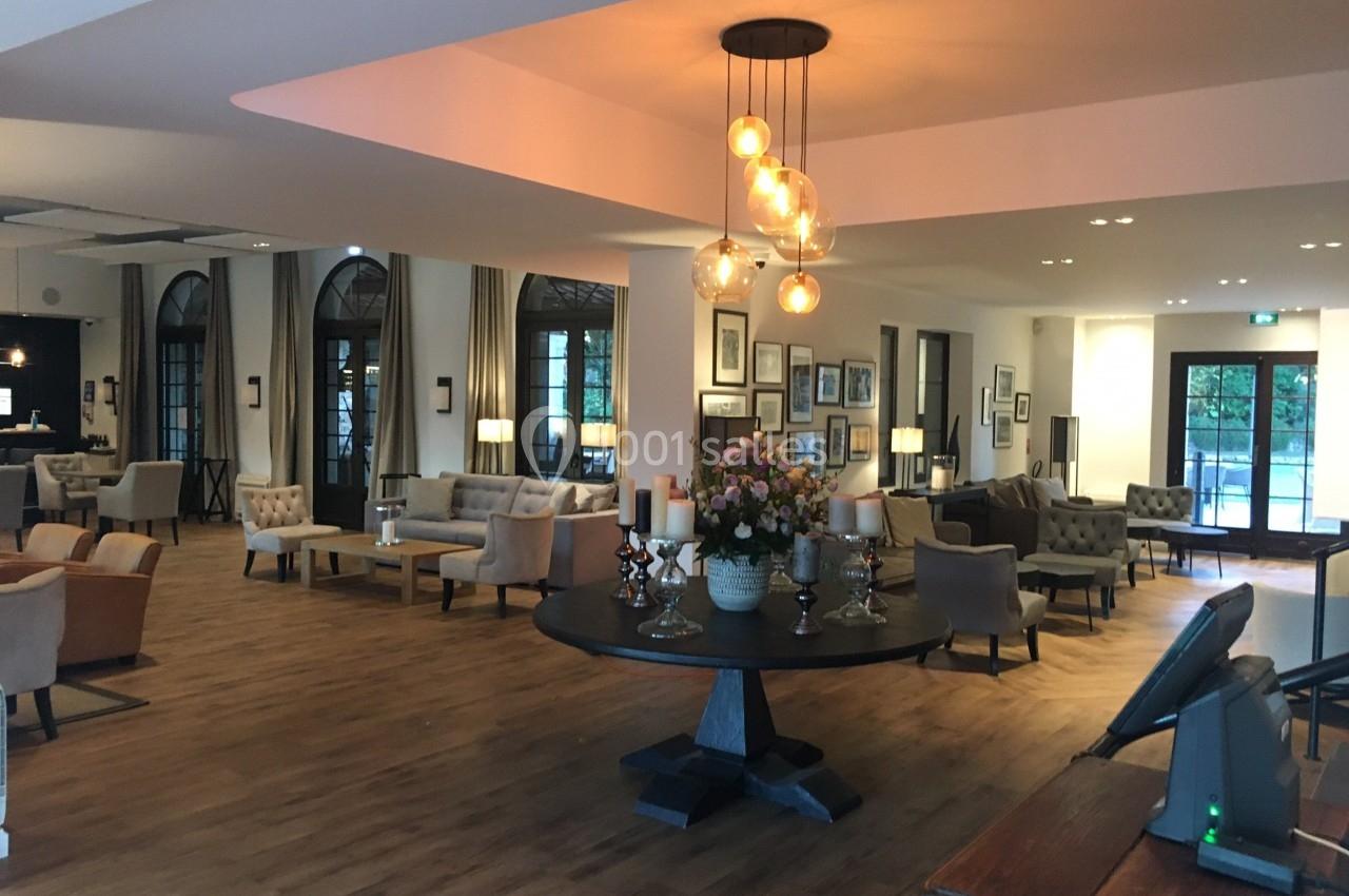 Salon spacieux avec parquet, mobilier élégant, table centrale décorée de fleurs et luminaires suspendus.