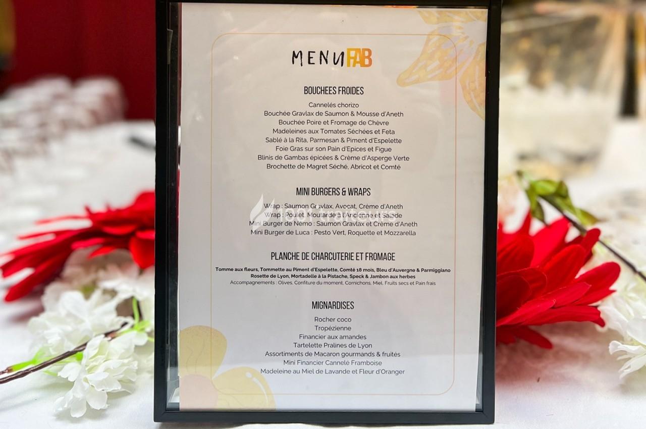 Carte de menu encadrée posée sur une table, entourée de fleurs rouges et blanches.