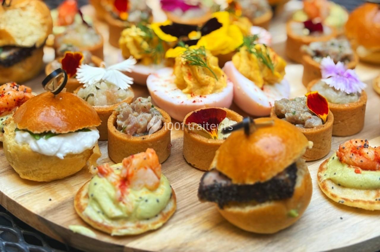 Plateau de bouchées apéritives variées comprenant mini-burgers, tartelettes, œufs farcis et décorations florales.