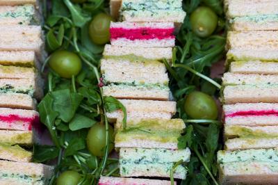Sandwiches colorés empilés avec des garnitures variées, entourés de roquette et d'olives vertes.