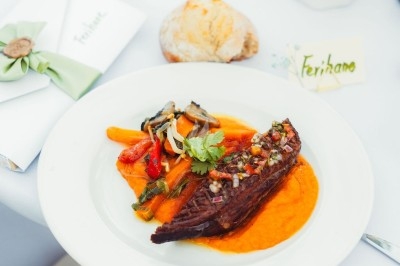 Assiette de viande grillée sur purée orange, accompagnée de légumes colorés, servie sur une table dressée.