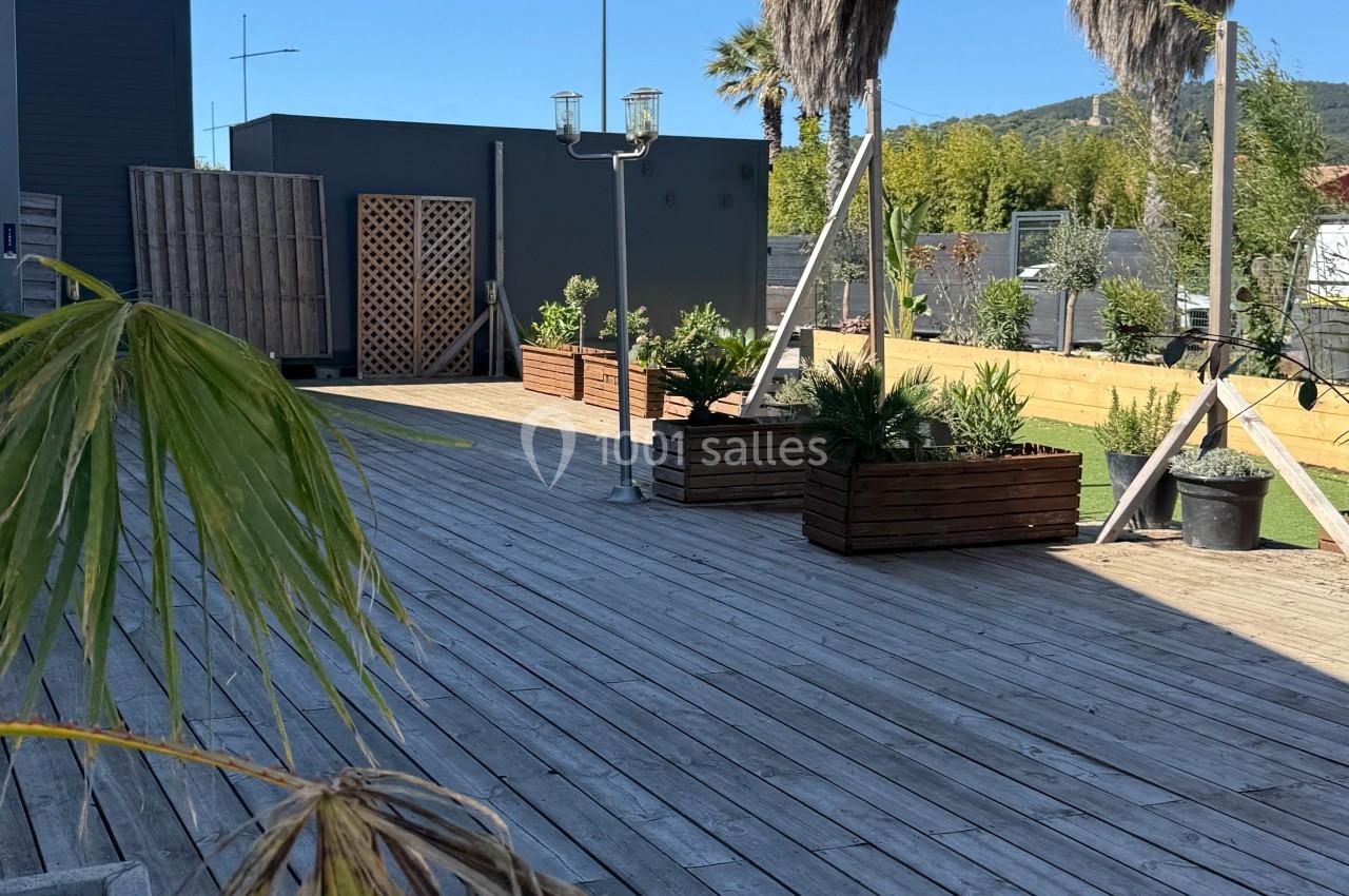 Terrasse en bois avec des bacs de plantes, deux palmiers et un ciel bleu dégagé en arrière-plan.