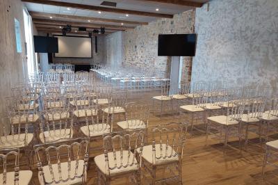 Des invités discutent debout dans un jardin devant une grande maison en pierre et une grange sous un ciel dégagé.