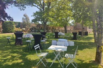 Des invités discutent debout dans un jardin devant une grande maison en pierre et une grange sous un ciel dégagé.