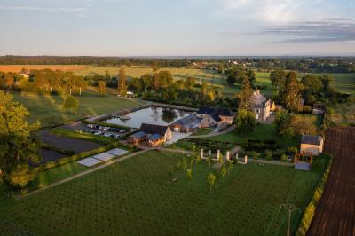 Des invités discutent debout dans un jardin devant une grande maison en pierre et une grange sous un ciel dégagé.
