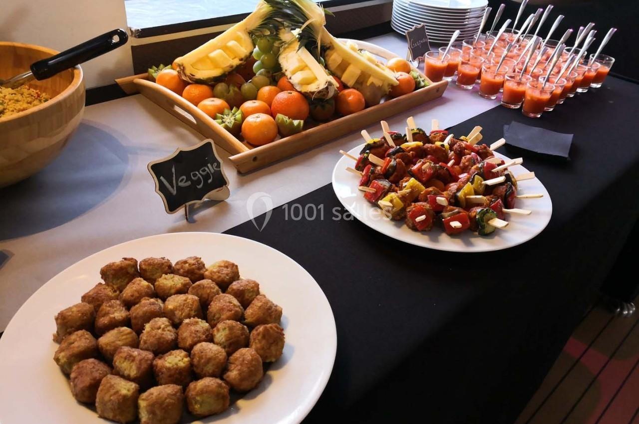 Buffet avec brochettes végétariennes, boulettes, fruits frais et verrines de soupe sur une table noire.