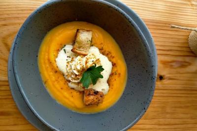 Bol de soupe de potiron garnie de croûtons, crème fraîche, persil et épices, posé sur une table en bois.