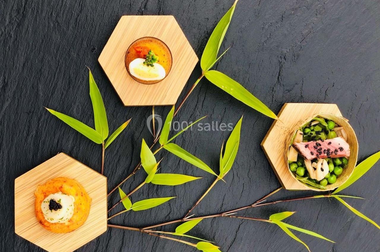 Assortiment de plats gastronomiques présentés sur des assiettes hexagonales en bois, décorés de feuilles de bambou.