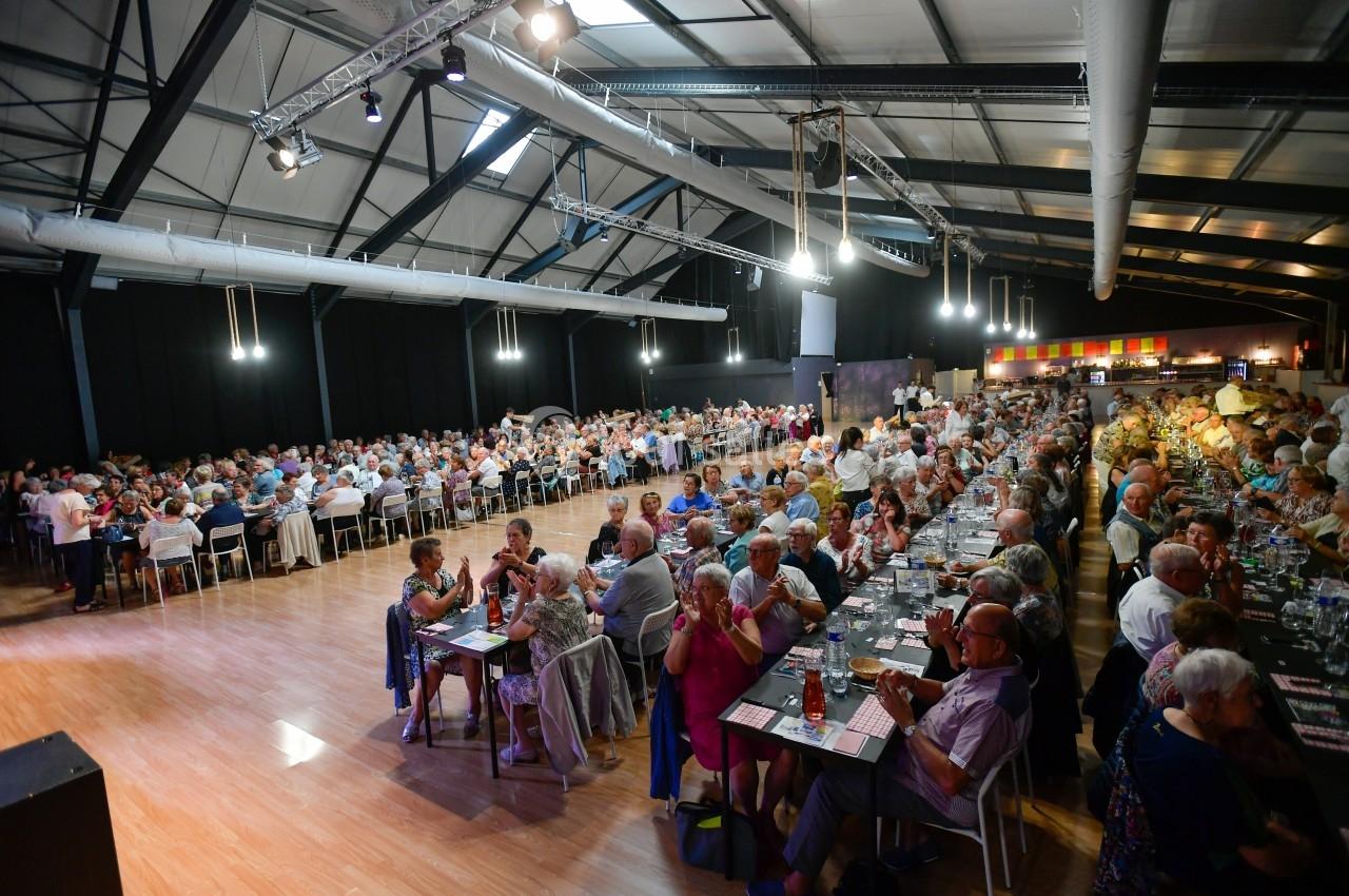 Salle comble avec de nombreuses personnes assises à des tables lors d'un grand repas ou événement collectif.
