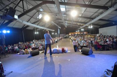 Un groupe de personnes photographiant un grand gâteau décoré, dans une salle remplie lors d'un événement festif.