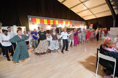 Un groupe de personnes photographiant un grand gâteau décoré, dans une salle remplie lors d'un événement festif.