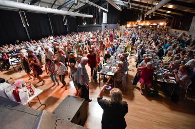 Un groupe de personnes photographiant un grand gâteau décoré, dans une salle remplie lors d'un événement festif.